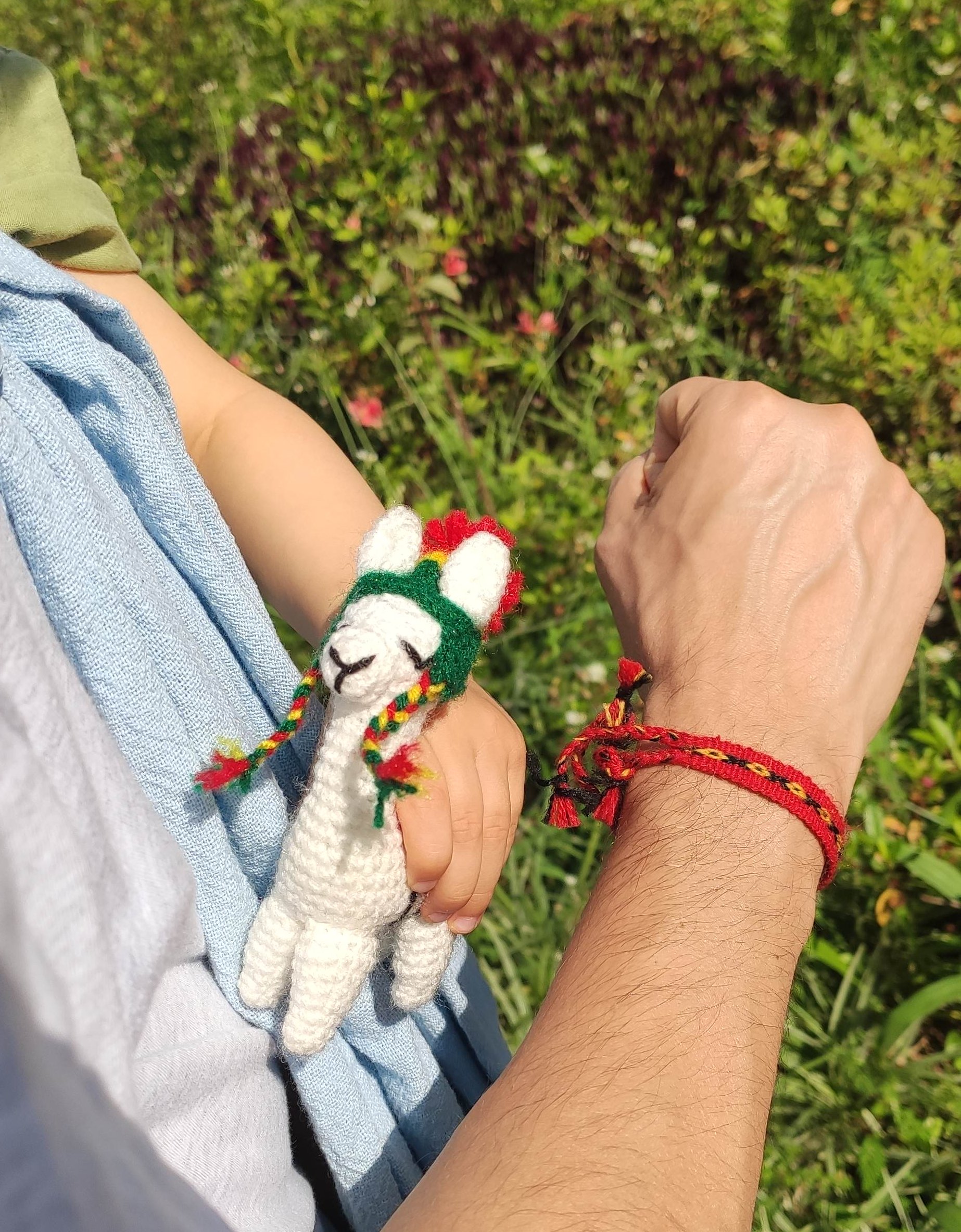 Pulseira de temática Boliviana em meu pulso e lhama de brinquedo na mão de um bebê